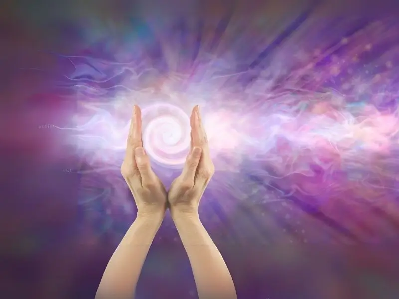 Zwei Hände mit lila Hintergrund und weißer Energiespirale in der Mitte. Symbolfoto