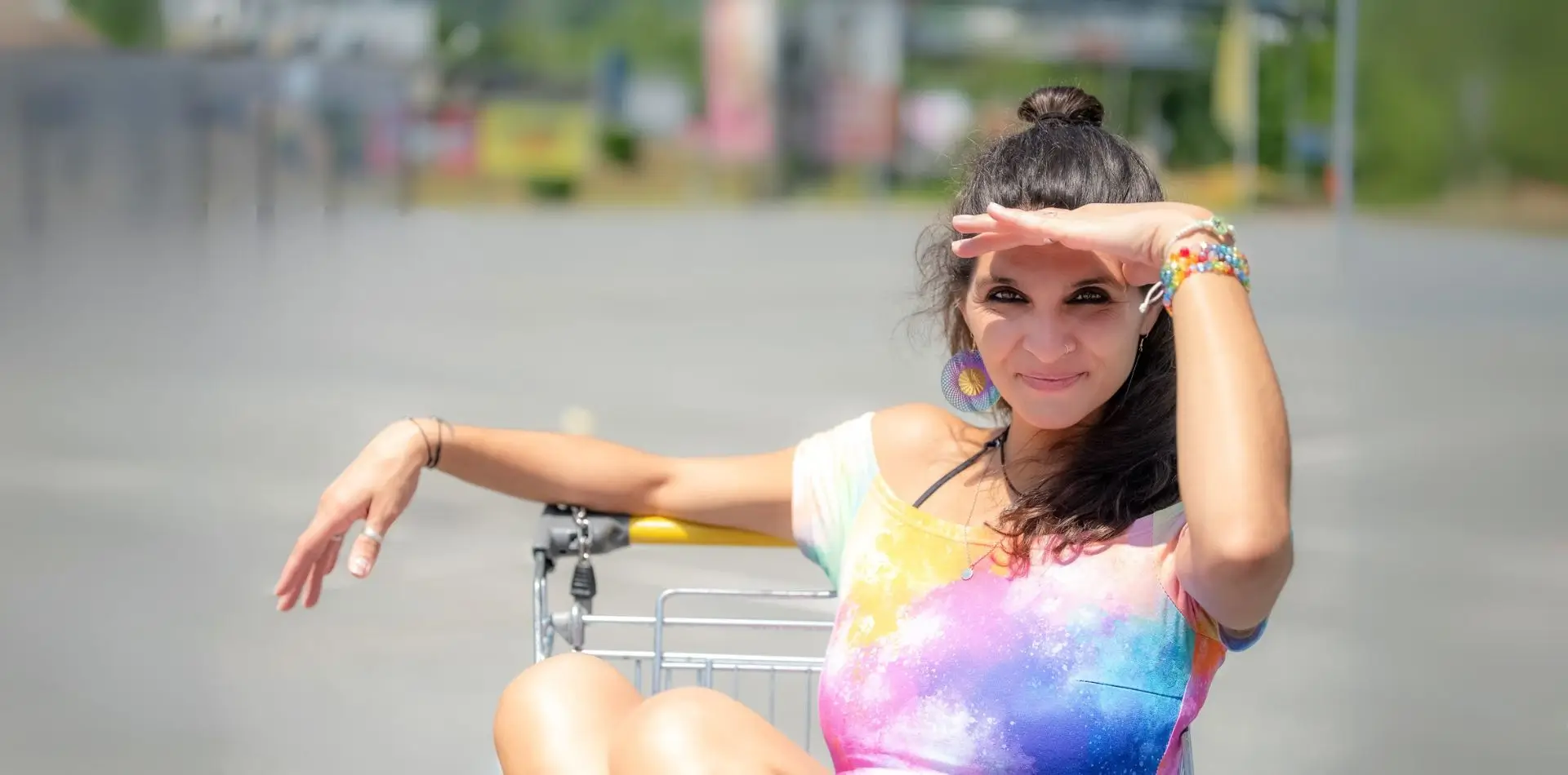 Martina Schatzl-Bachträgl lächelnd und mit der linken Hand über den Augen, um diese vor der Sonne zu schützen. Sie sitzt dabei in einem Einkaufwagen.