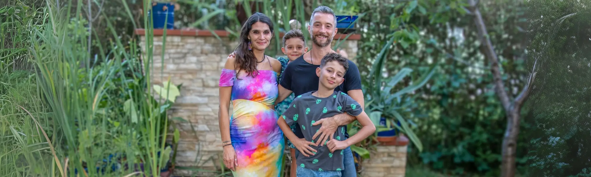 Familie Schatzl-Bachträgl in ihrem Garten in Graz Seiersberg. Martina und ihr Mann Robert sind darauf mit ihren beiden Söhnen zu sehen. Rundum ist sehr viel Grün im Bild.