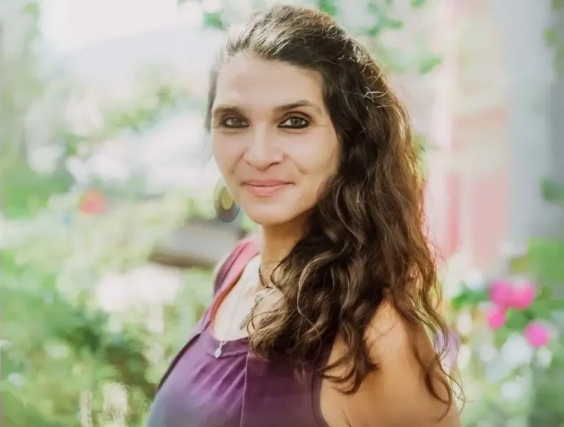 Profilbild von Martina Schatzl-Bachträgl vor grün-buntem Natur-Hintergrund mit offenen und leicht gewellten dunklten langen Haaren. Sie blickt ruhig, leicht lächelnd und mit geschlossenem Mund in die Kamera.