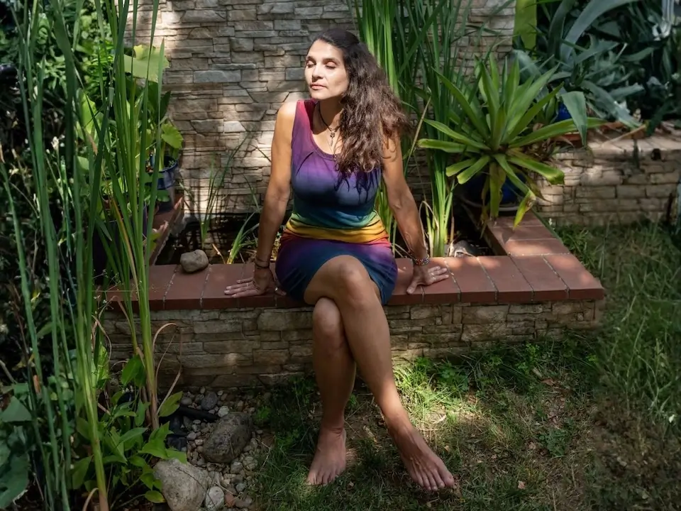 Frau im Garten ohne Schuhe mit geschlossenen Augen auf kleiner Ziegelmauer